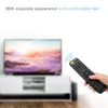 A hand holding a remote control in front of a blurred television and entertainment center. Voir les images du produit