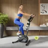 A woman is exercising on a stationary bike in a modern living room. Produktbild-Vorschau