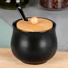 A black ceramic sugar bowl with a wooden lid and a small spoon, placed on a wooden surface. Produktbild-Vorschau