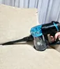 A hand holding a blue and black cordless vacuum cleaner with a crevice tool attached, resting on a beige couch. Podgląd zdjęcia produktu