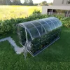 A greenhouse in a garden setting, with a modern building in the background and a field of yellow flowers. Anteprima dell’immagine prodotto