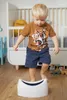 A young boy is standing in front of a white potty training seat in a nursery. Náhľad obrázku produktu