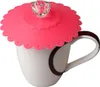 A pink silicone cup lid with a clear diamond-shaped embellishment sits on top of a white mug with a brown rim and handle. Produktbild-Vorschau