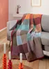 A colorful plaid blanket draped over a sofa, with candles in the foreground. Anteprima dell’immagine prodotto