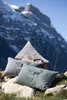 Three decorative pillows with deer motifs are arranged on rocks and a sheepskin in front of a snow-capped mountain range. Produktbild-Vorschau