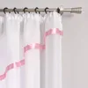 A close-up view of white sheer curtains with pink ribbon accents hanging from a curtain rod. Produktbild-Vorschau