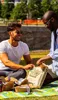 Two men are having a picnic in a park, opening a bag of food. Produktbild-Vorschau