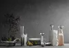 A collection of modern kitchenware and decorative items arranged on a gray surface against a dark gray textured wall. Produktbild-Vorschau
