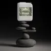 A white plastic jug of Roxlin binding agent for gravel stones is balanced on a stack of smooth, dark gray stones against a dark background. Produktbild-Vorschau