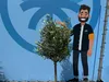 A cartoon character stands next to a small olive tree in front of a blue backdrop with a large circular graphic. Produktbild-Vorschau