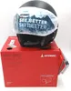 A black ski helmet with a protective cover featuring mountain graphics and text, placed on top of its red retail box. Náhled obrázku produktu