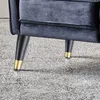 A close-up view of the bottom part of a dark gray velvet chair, showing its black legs with gold accents. Produktbild-Vorschau