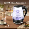 A glass electric kettle with blue illuminated water is shown on a wooden table, with a cup of coffee and sugar cubes nearby. The background depicts a kitchen setting. Produktbild-Vorschau