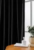 A black curtain hangs in front of a window, with a small plant and a decorative object on a table in the foreground. Produktbild-Vorschau