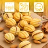 A collection of nut-shaped cookies filled with a dark filling, arranged on a brown surface with cinnamon sticks and almonds scattered around. Three yellow square icons with illustrations are at the top. Voir les images du produit