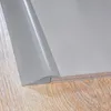 A close-up view of a gray PVC transition profile laid on a wooden floor and a plywood substrate. Anteprima dell’immagine prodotto