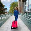 A woman is walking with a red shopping trolley on a walkway next to a modern building. Voir les images du produit