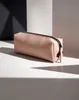 A pink accessory case with a black zipper is placed on a white surface with dramatic shadows. Voir les images du produit