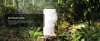 A silver and white air conditioning unit is placed on a tree stump in a lush forest setting. Produktbild-Vorschau