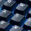 A close-up shot of a black gaming keyboard with illuminated blue backlighting. Produktbild-Vorschau