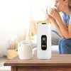 A woman drinks from a mug while a white electric kettle sits on a table next to a glass jar of milk. Produktbild-Vorschau