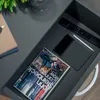 A close-up view of a drawer in a nightstand, containing a book, a tablet, and a remote control. Produktbild-Vorschau