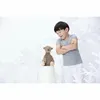 A young boy looks down at a teddy bear sitting on a white bucket, with white decorative branches in the background. Podgląd zdjęcia produktu