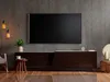 A modern living room with a TV console and a large television mounted on a concrete wall. Produktbild-Vorschau