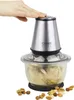 A hand pressing down on the lid of a food chopper, with chopped food inside the glass bowl and nuts scattered around the base. Produktbild-Vorschau