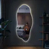 A bedroom scene with a large, irregularly shaped mirror with LED lighting mounted on the wall. Produktbild-Vorschau