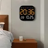 A digital clock is mounted on a wall above a nightstand with a mug on it. Produktbild-Vorschau
