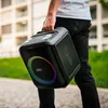 A person is holding a portable speaker outdoors. Produktbild-Vorschau