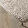 A close-up view of the textured fabric of a beige bar stool, with a wooden floor visible in the background. Produktbild-Vorschau