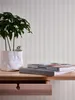 A plant in a white pot sits on a wooden shelf next to two books. Produktbild-Vorschau