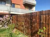A bamboo fence in a garden with a building in the background. Náhľad obrázku produktu
