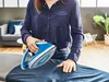 A person is ironing clothes in a living room setting. Produktbild-Vorschau