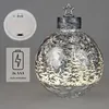 A decorative Christmas bauble with a winter forest scene and LED lights, shown with its battery compartment and a battery indicator icon. Produktbild-Vorschau