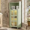 A green corner cabinet with glass doors and internal lighting is shown in a bathroom setting next to a window. Produktbild-Vorschau