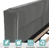 Close-up of a gray upholstered bed frame with wooden slats visible underneath. Four teal-colored badges with icons and text are displayed at the bottom. Produktbild-Vorschau