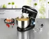 A black stand mixer with a stainless steel bowl filled with batter, placed on a kitchen counter next to a bundt cake and berries. The mixer comes with accessories like a whisk and dough hook.