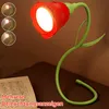 A red rose-shaped desk lamp with a green stem and leaves is shown on a desk next to a book. There are also three small circular insets showing different lighting effects of the lamp. Produktbild-Vorschau