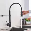 A black kitchen faucet with a pull-down sprayer is shown in use, with water running into a sink. A hand is visible operating the faucet. Náhľad obrázku produktu