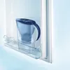 A blue water filter pitcher sits on a shelf inside a refrigerator. Produktbild-Vorschau