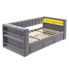 A gray upholstered daybed with a slatted mattress base and integrated shelving on one side. The headboard has tufted detailing, and there is a yellow LED light strip at the back of the headboard. Náhľad obrázku produktu