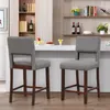 Two gray bar stools with wooden legs are placed in front of a white counter in a kitchen or dining area. Produktbild-Vorschau