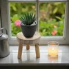 A small wooden stool with a potted succulent plant and a lit candle on a windowsill. Produktbild-Vorschau