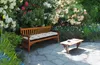 A garden bench with a cushion and a coffee table on a stone patio, surrounded by blooming flowers. Podgląd zdjęcia produktu