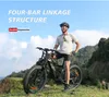 A man is posing with an electric mountain bike on a grassy hillside with a scenic view of mountains and sky. Produktbild-Vorschau