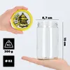 A hand holding a lid with a bee hive design, and a glass jar being held in another hand, with dimensions and weight indicated. Produktbild-Vorschau