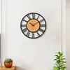 A wall clock with Roman numerals hanging on a white wall. Produktbild-Vorschau